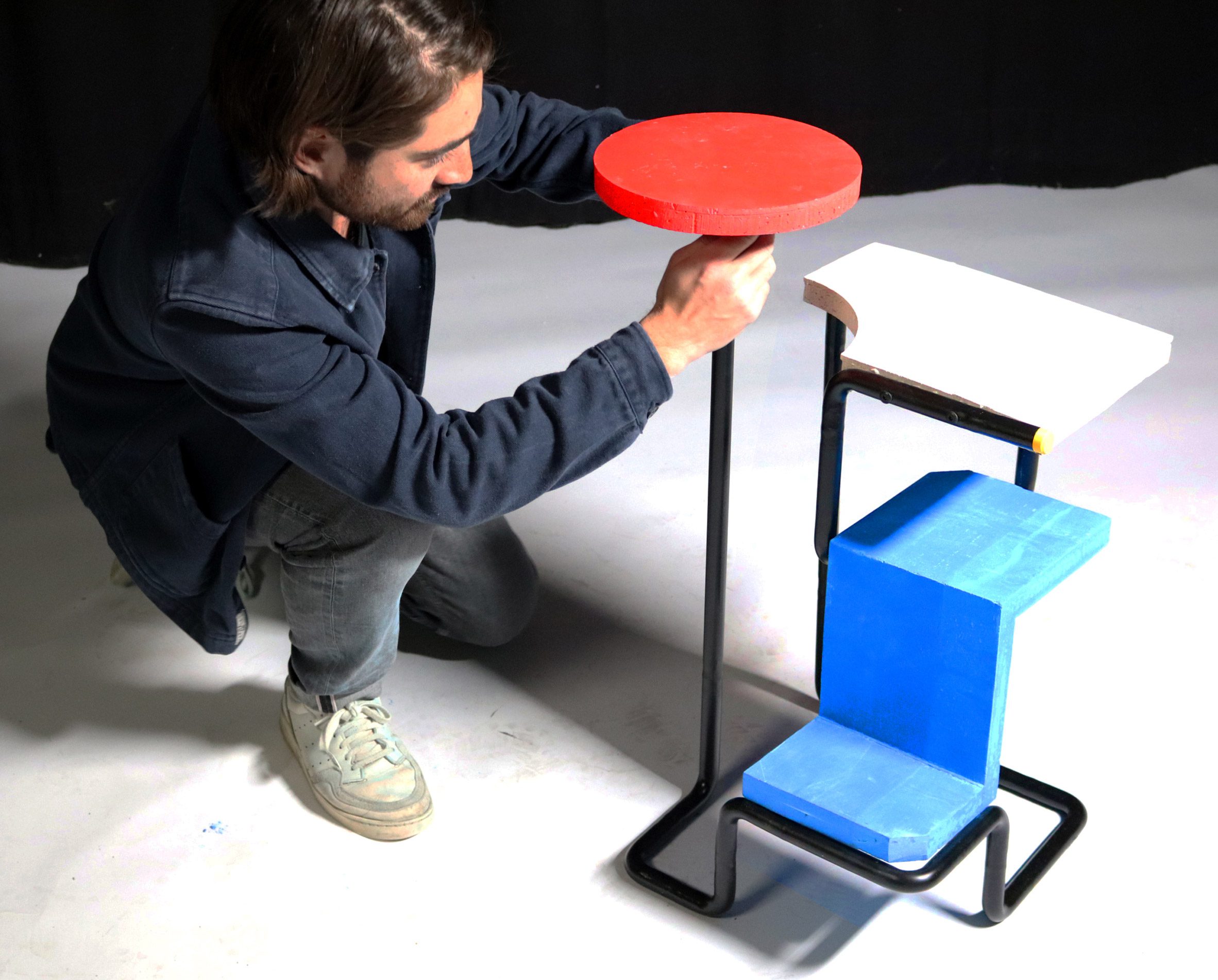 Person handling a side table with red, white and blue tabletops and a metal structure made from stool legs.